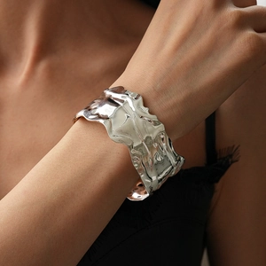 Detail of silver wavy crumpled wide cuff bracelet on wrist with black lace sleeve