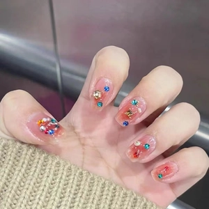 Detail of pink cat-eye press-on nails with colorful rhinestones and gold beads