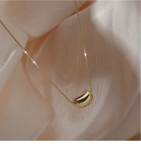 Detail of polished gold bean pendant on a delicate box chain with silk background