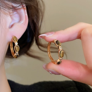 Close-up of gold plated earring with tiger eye stone and zircons on ear
