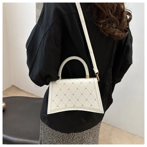 Detail of white quilted handbag featuring gold studs and woven handle on a model