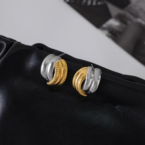 Detailed macro shot of two-tone gold and silver twisted huggie earrings on black leather
