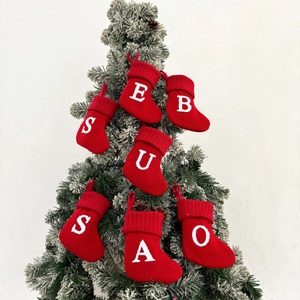 Red and white knitted Christmas stockings with alphabet letters hanging on a snowy tree