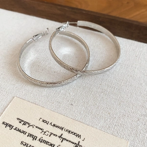 Close-up of silver hoop earrings with textured finish on a rustic linen background