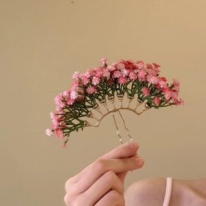 Close-up of a golden fan-shaped hairpin with pink baby's breath floral decorations