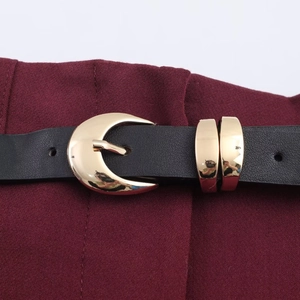Macro detail of high-waist trousers featuring a black faux leather belt and gold crescent buckle