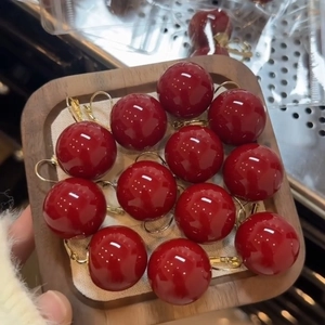 Elegant red resin sphere drop earrings with gold metal hooks on a wooden display tray