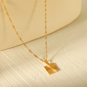 Close-up of golden square pendant on a water wave chain against a textured beige background