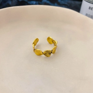 Detail eines goldenen verstellbaren Rings mit geprägtem Blattmuster auf Keramikteller