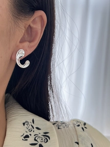 Close-up of minimalist silver C-shaped polished metal stud earring on a model
