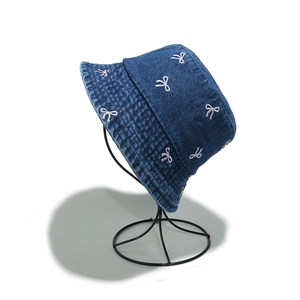 Detailed view of dark blue denim bucket hat with white embroidered bows and wide brim