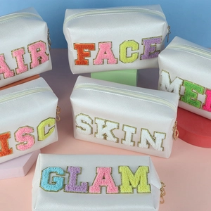 Close-up of white PU leather makeup bags featuring chenille letters and gold glitter edges