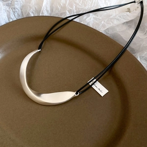 Macro detail of crescent metal pendant featuring a brushed matte silver finish on a cord