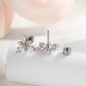 Silver snowflake earrings with cubic zirconia stones and screw back studs on white surface