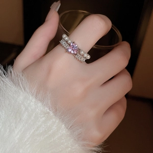 Détail d'une bague coeur avec zircon rose, perles et placage argent sur un doigt
