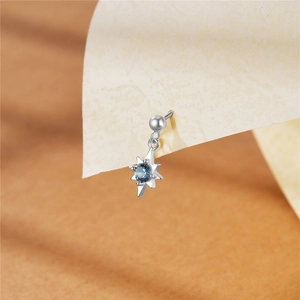 Macro shot of silver star-shaped earring featuring a blue zircon stone on textured paper