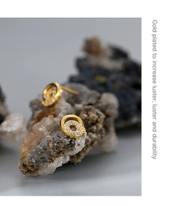Macro view of gold plated hoop earrings with cubic zirconia on a natural rock texture