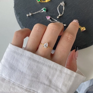 Close-up of a gold chain ring with pear-shaped clear zircon on a model's hand