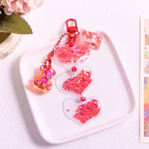 Detail of red glitter keychain with bear and heart charms on a white display tray