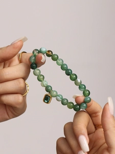 Detail of green agate beaded bracelet with a gold-bordered emerald square pendant on wrist