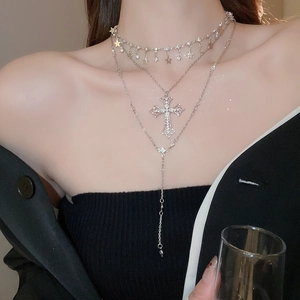 Close-up of layered silver necklace with sparkling cross and star pendants on neck