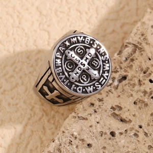Macro shot of silver retro St. Benedict cross ring on a textured stone surface