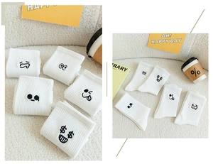 Detail of white cotton socks featuring black cartoon emoji embroidery and ribbed cuffs