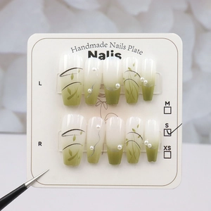 Détail de faux ongles dégradés vert et blanc avec motifs de feuilles et petites perles
