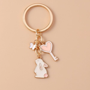 Close-up of golden keychain with white enamel rabbit, pink heart, and butterfly charms