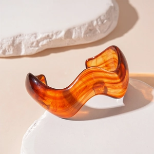 Detailed view of an irregular wavy amber resin cuff bracelet on white stone