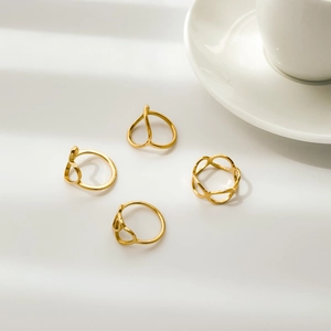 Detail of four gold geometric hollow heart rings on a white textured background