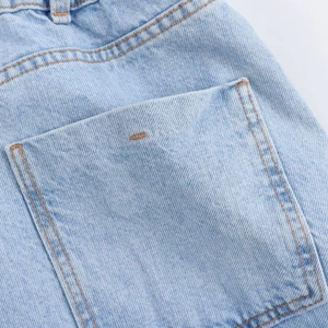 Detailed close-up of light blue denim romper rear pocket with orange contrast stitching