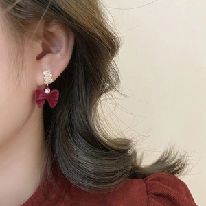 Gros plan d'une boucle d'oreille nœud en velours bordeaux avec dorure et strass brillants
