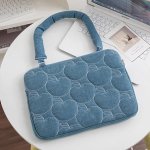 Détail de la housse pour ordinateur en denim bleu avec broderie pomme et poignées