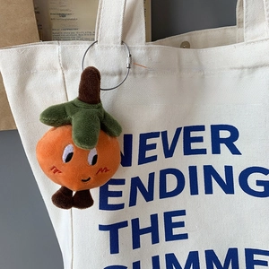 Detail of cute orange plush charm attached to white canvas bag with a metal screw ring