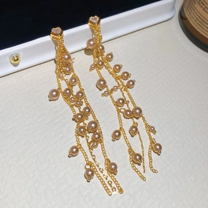 Dettaglio di eleganti orecchini a nappa dorata con perle champagne e perni in zircone a cuore