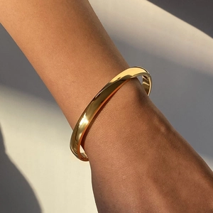 Close-up of polished gold stainless steel bangle with a minimalist clasp worn on wrist