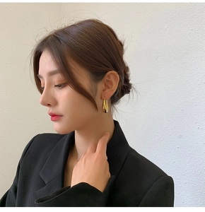 Golden teardrop earrings in polished titanium steel on a model wearing a black blazer