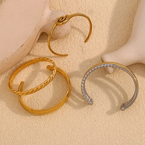 Polished stainless steel bracelets in gold and silver set against a warm sandy background
