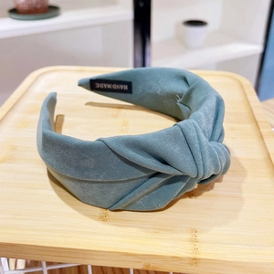 Detail of teal twisted fabric headband featuring handmade label on a wooden tray