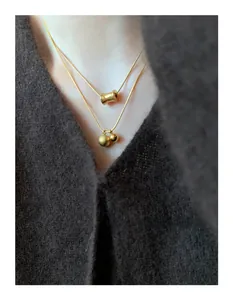 Close-up of double-layer gold snake chain necklace with cylindrical and ball pendants