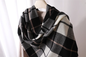 Detail of soft black, white, and beige plaid scarf with fringes on a wooden hanger