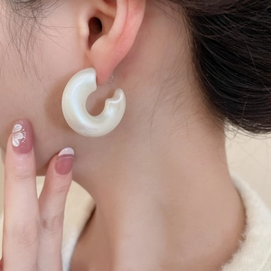 Close-up of pearl white chunky C-shaped acrylic earrings worn with elegant styling