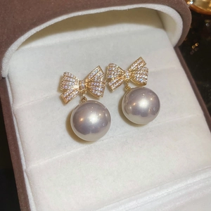Nahaufnahme goldener Schleifenohrringe mit funkelnden Diamanten und hängenden Perlen