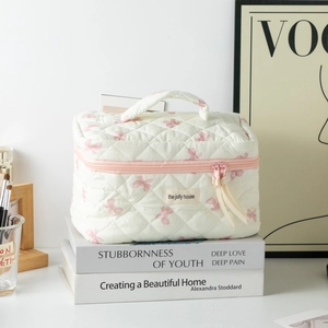 Detailed close-up of cream quilted cosmetic bag with pink bow pattern and top handle
