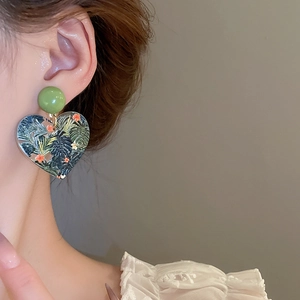 Detail of heart-shaped acrylic earrings with tropical leaf patterns and green bead studs