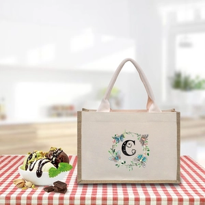 Detail view of beige canvas tote bag featuring floral butterfly wreath and black letter C