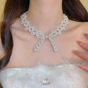 Close-up of elegant woven pearl bow necklace on model with white fluffy clothing