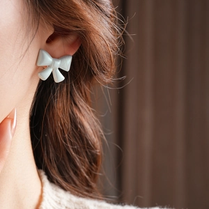Detail view of light blue acrylic bow stud earrings with a matte finish on model