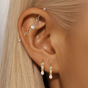 Macro shot of silver industrial barbell earring with chain and gold zircon hoops